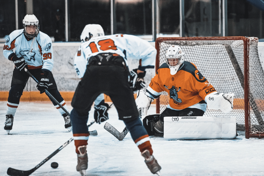 Three ice hockey players wearing orange, black and white jerseys